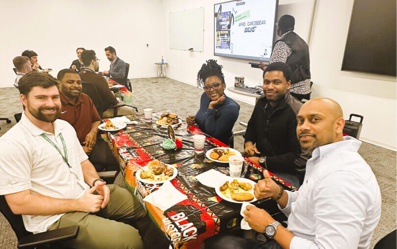 A group of colleagues enjoying a meal together at a decorated table during an Afro-Caribbean Black History Month celebration in a meeting room setting.