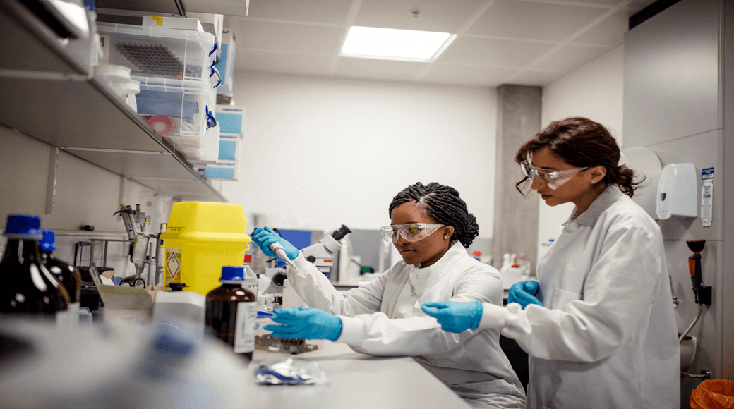 Scientists performing cell therapy research in a GMP-compliant biotechnology lab using pipettes and laboratory equipment.