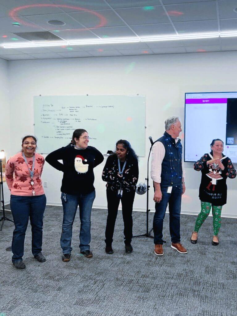 Cellipont team members smiling and standing in a decorated office space, wearing holiday sweaters and festive attire.